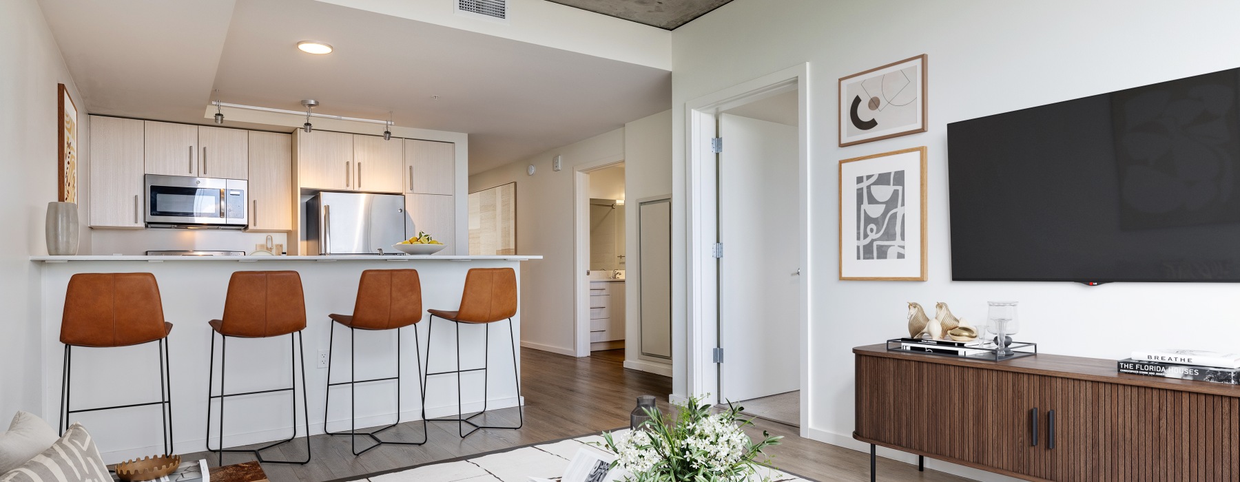 Living room with TV and four leather stools at kitchen counter 